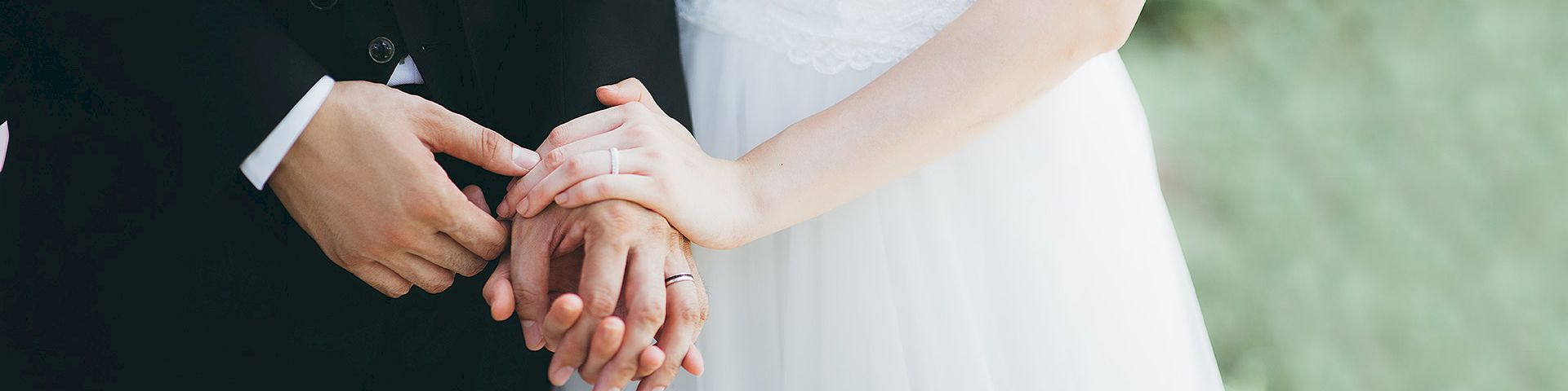 Two hands with rings join in a wedding moment, a bride and groom holding each other&rsquo;s fingers.