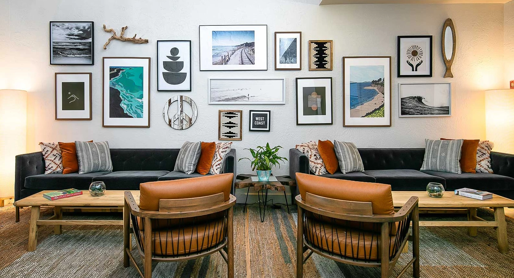 Cozy modern lounge with a gallery wall, two black sofas, orange-brown leather chairs, wooden coffee tables, and warm lighting.