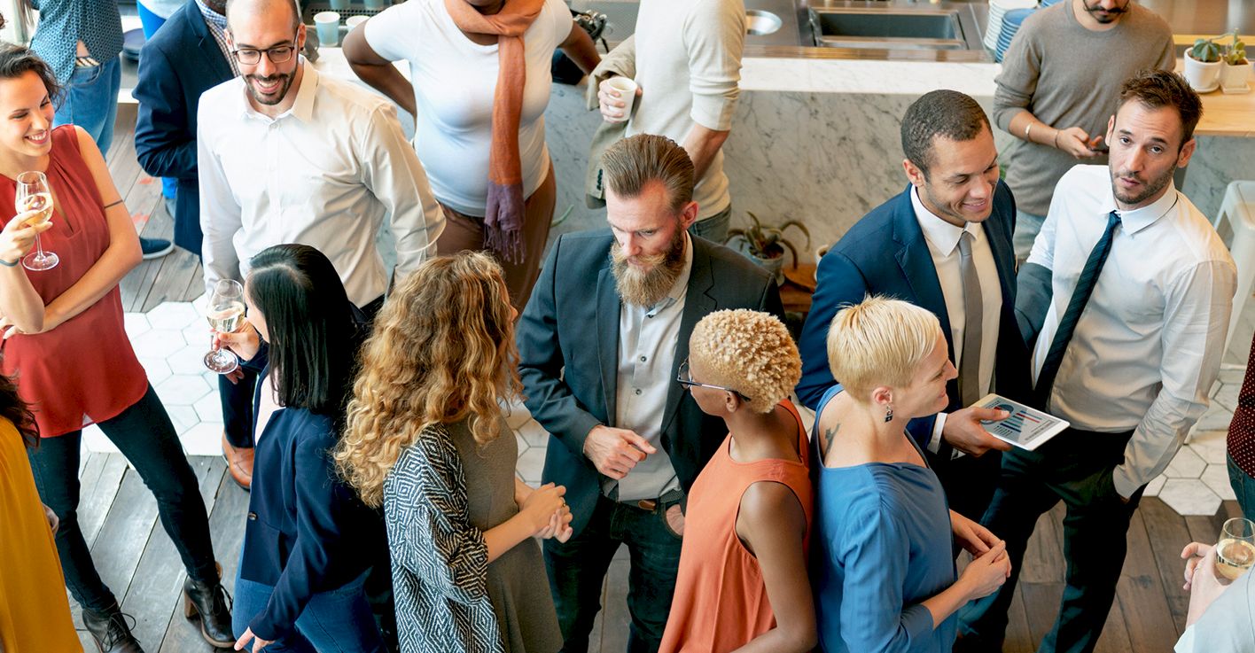 A busy, diverse group of professionals mingling at a modern office or conference, chatting and networking in a social setting.