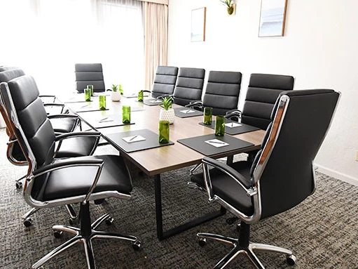 A modern conference room with a long table, black leather chairs, green bottles and notepads set for a meeting. End.