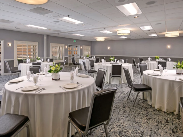 A banquet hall set for a formal event with round tables, white tablecloths, place settings, and small green plant centerpieces.
