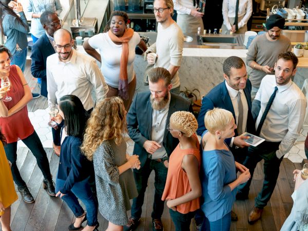 A diverse group of professionals socializes in a modern office lobby, chatting, networking, and grabbing drinks.