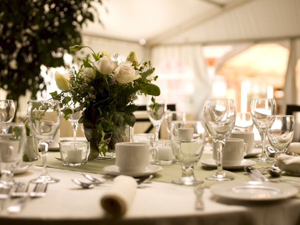 A formal dining table set with white flowers centerpiece, multiple place settings, and glassware ready for a meal at a fancy event.