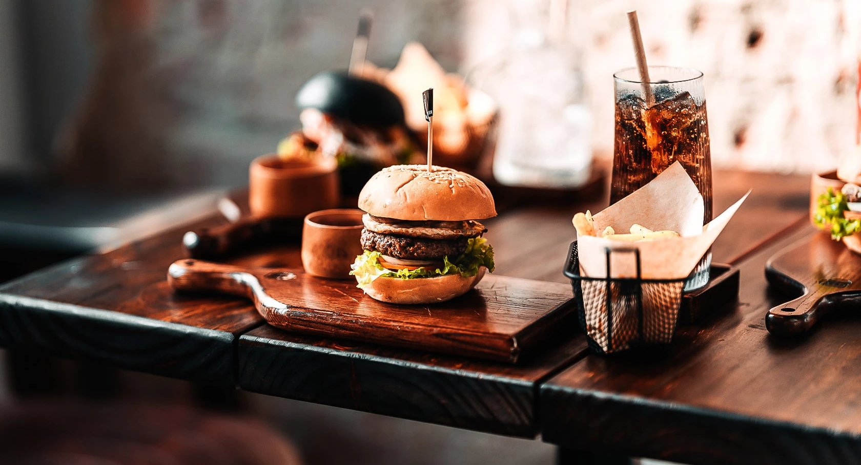 A burger meal with fries and a drink on a rustic wooden table, set against a warm, moody restaurant background.