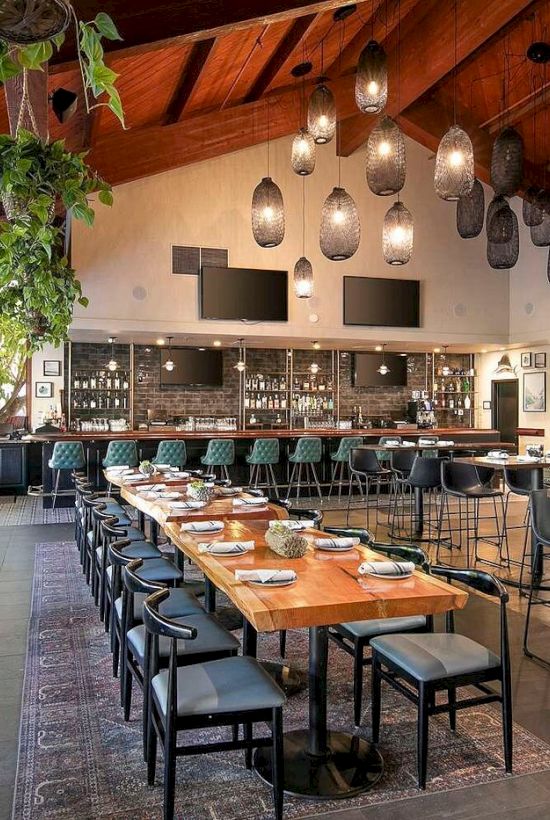A modern restaurant/bar interior with a long wooden table, blue chairs, pendant lights, and a stocked back bar.