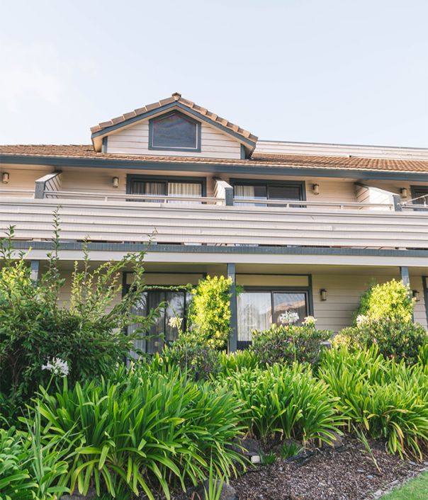 A two-story house with a manicured front yard and green shrubbery, under a clear sky, with a small gable above the windows.