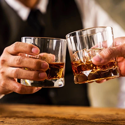 Two people clinking whiskey glasses in a toast, close-up on hands and amber liquid.