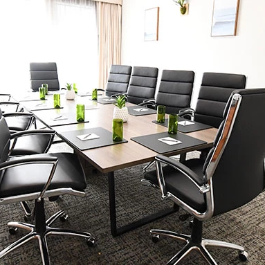 A modern conference room with a long table, black leather chairs, plants, water bottles, and notebooks set for a meeting.